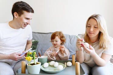 Lächelnder Vater betrachtet Frau, die zu Ostern ein Ei von ihrer Tochter färbt - VYF00519