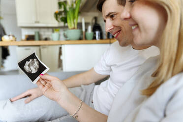 Smiling husband and wife looking at ultrasound picture at home - VYF00539