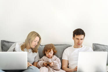 Geschäftsfrau mit Laptop, die ihre Tochter mit dem Mobiltelefon eines Geschäftsmannes beobachtet, der zu Hause arbeitet - VYF00542