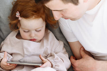 Father looking at daughter with mobile phone at home - VYF00548