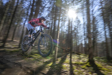 Männlicher Sportler in der Luft mit Mountainbike im Wald - RNF01322