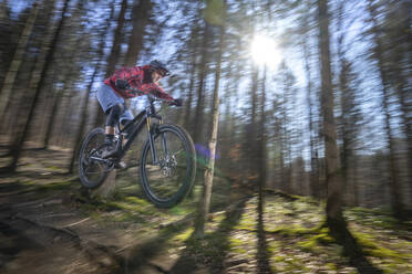 Male athlete in mid-air with mountain bike in forest - RNF01322