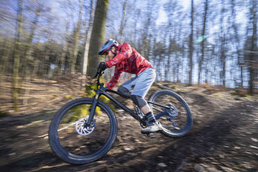 Mann fährt Mountainbike auf unbefestigtem Weg im Wald - RNF01323