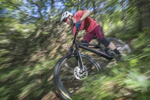 Male athlete moving down while riding bicycle in forest - RNF01325