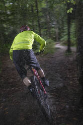 Mann fährt Fahrrad auf unbefestigtem Weg im Wald bei Regen - RNF01326