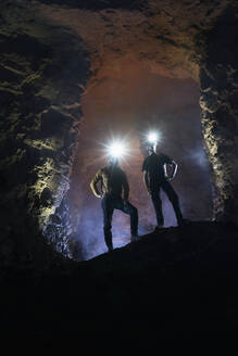 Male tourists exploring cave wearing illuminated headlamps - RNF01342
