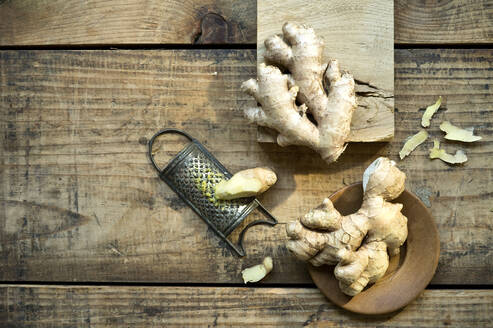 Ginger roots and old grater lying on wooden surface - ASF06745