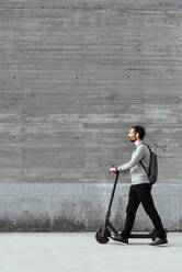 Man walking near electric scooter in front of grey wall - CAVF93767