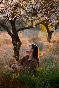 Porträt einer jungen Frau, die bei Sonnenuntergang auf hohen Gräsern sitzt - CAVF93772