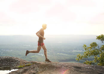 Erwachsener männlicher Trailrunner auf einem Bergkamm bei Sonnenuntergang - CAVF93856