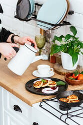 Women's hands pour tea into a cup. cheese pancakes with jam on a - CAVF93865