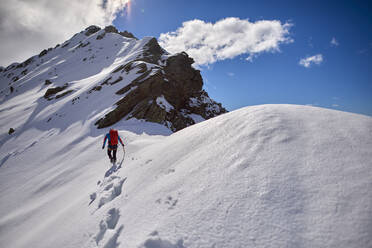 Ein Mann besteigt an einem sonnigen Tag einen verschneiten Berg in Devero, Italien. - CAVF93883