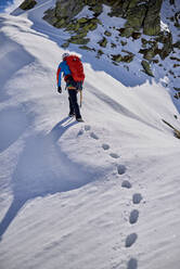 Man climbing a snowy mountain on a sunny day in Devero, Italy. - CAVF93884