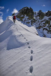Ein Mann besteigt an einem sonnigen Tag einen verschneiten Berg in Devero, Italien. - CAVF93885