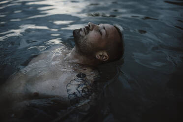 Hipster Mann mit geschlossenen Augen entspannt im Meer - GMLF01154