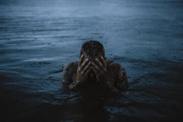 Mann berührt Gesicht im Meer bei Regen - GMLF01158