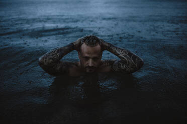 Hipster Mann mit Händen hinter dem Kopf im Meer im Regen - GMLF01159