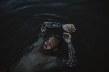Mann mit geschlossenen Augen schwimmt auf Wasser im Meer - GMLF01160