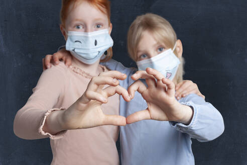 Sisters machen Herzform mit Händen tragen Gesichtsmaske gegen schwarzen Hintergrund - GAF00152