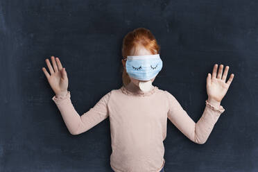 Redheaded girl with face mask holding biscuit in mouth against black background - GAF00156