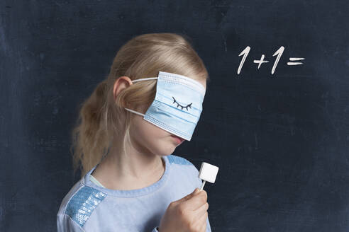 Mädchen, das einen Lutscher hält und sein Gesicht mit einer Maske vor einem schwarzen Hintergrund mit einem Matheproblem bedeckt - GAF00160