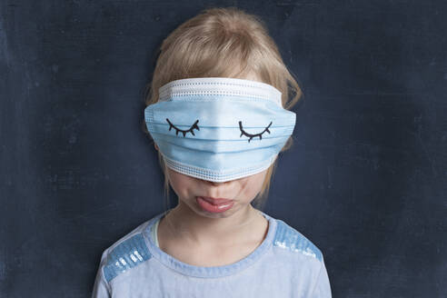 Displeased girl with wearing face mask on eyes against black background - GAF00161
