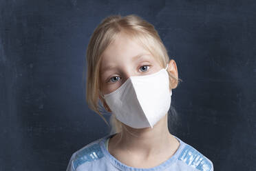 Girl with cocked head wearing protective face mask against black background - GAF00163