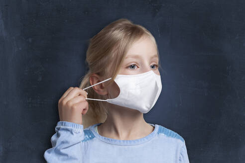 Girl pulling string of face mask against black background - GAF00164