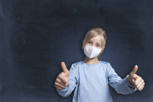 Girl showing thumbs up gesture wearing face mask against black background - GAF00167