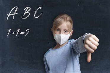 Girl showing thumbs down gesture wearing face mask against black background with alphabets and maths problem - GAF00168