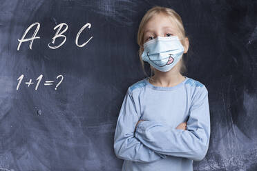 Girl with arms crossed wearing face mask by black background with alphabets and maths problem - GAF00169