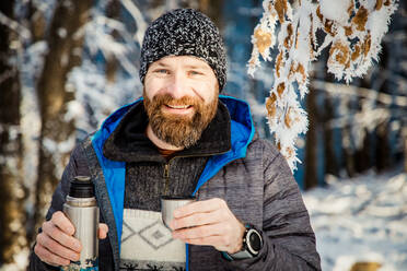 Man drinking hot tea in winter forest - CAVF93931
