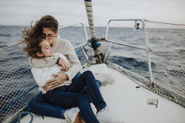 Mother kissing daughter while sitting on sailboat - GMLF01165