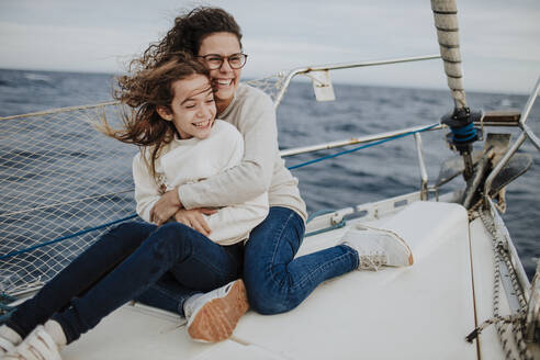 Cheerful mother embracing daughter while traveling on sailboat - GMLF01167