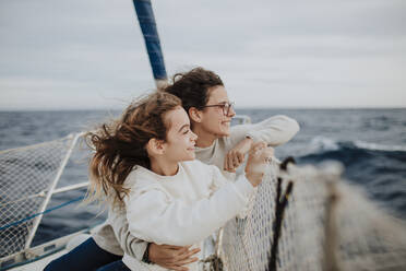 Mother and daughter looking at view while traveling on sailboat during vacation - GMLF01168