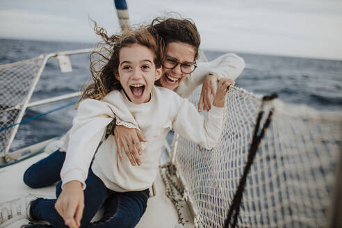 Laughing mother with excited daughter on sailboat during vacation - GMLF01169