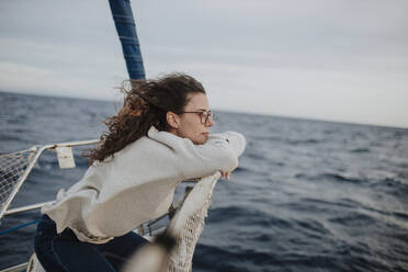 Nachdenkliche Frau, die wegschaut und sich auf ein Segelboot stützt - GMLF01174