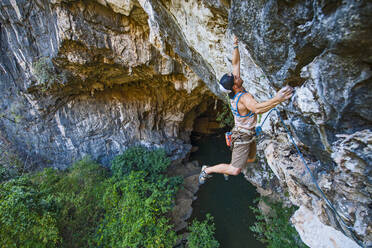 Mann klettert auf überhängendem Kalksteinfelsen in Laos - CAVF93960