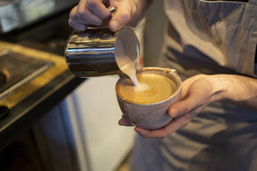 Barista gießt Milch in Kaffee im Café - FBAF01809