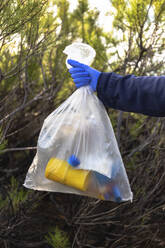 Woman wearing protective glove holding plastic garbage bag - JPTF00748