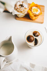 Top view Zusammensetzung der süßen Schokolade Bomben schmelzen in Glas frischer heißer Milch auf dem Tisch in der Nähe von leckeren Cupcakes und Milchkännchen platziert - ADSF22702