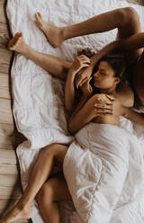 From above content relaxed female lying on fit boyfriends legs on soft cozy blanket on wooden floor - ADSF22725