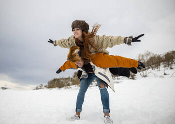 Fröhlicher männlicher Tourist trägt seine Freundin mit erhobenen Armen huckepack auf einem verschneiten Berg im Winter - ADSF22734
