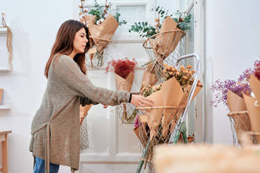 Seitenansicht einer Kundin, die einen Blumenstrauß aus einem Behälter nimmt, während sie im Geschäft eine Auswahl trifft - ADSF22758