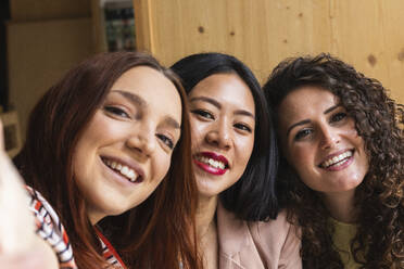 Young women taking selfie through mobile phone together at cafe - PNAF01400