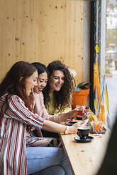 Freundinnen benutzen ein Mobiltelefon, während sie im Café sitzen - PNAF01402