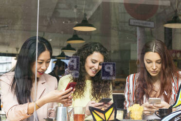 Junge Frauen benutzen Mobiltelefone in einem Cafe - PNAF01403