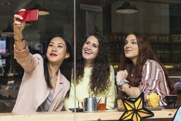Junge Frau nimmt Selfie mit weiblichen Freunden durch Handy im Cafe - PNAF01404