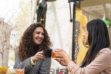 Lächelnde Frauen stoßen mit einem Getränk in einem Straßencafé an - PNAF01408