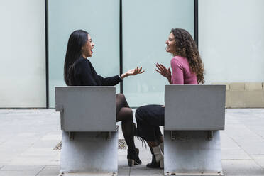 Junge Frauen, die auf einer Bank sitzend miteinander reden - PNAF01418